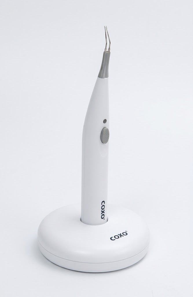 A white COKO dental laser pen device with a curved metal tip, standing upright on a matching white charging base against a clean white background.